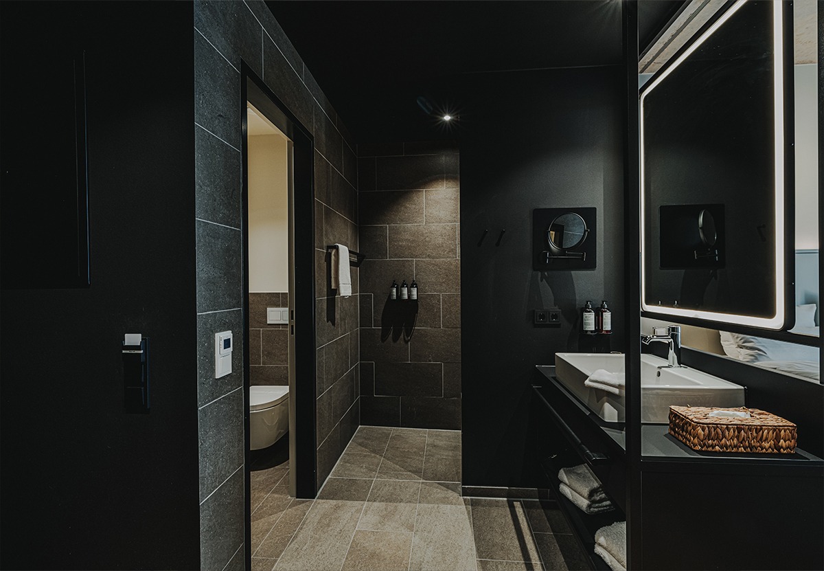 Die dunklen Fliesen verleihen den Badezimmern eine zeitlose Eleganz und eine moderne Ästhetik, während die weiße Sanitärkeramik als Eyecatcher heraussticht.Foto: HIIVE Hotels Group GmbH 